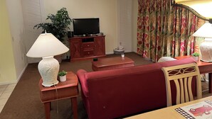A living room with a sofa, a TV on a wooden cabinet, a lamp, and a plant. - TimeOut 2!  Spacious 2 bed/2bath condo, Sleeps 6, Pool! (Mulberry)
