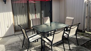 A patio with a glass table and four chairs, a red umbrella, and a white fence. - TimeOut 2!  Spacious 2 bed/2bath condo, Sleeps 6, Pool! (Mulberry)