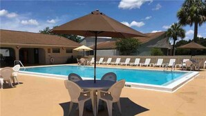 A pool area with lounge chairs and umbrellas, a pool table, and a building in the background. - TimeOut 2!  Spacious 2 bed/2bath condo, Sleeps 6, Pool! (Mulberry)
