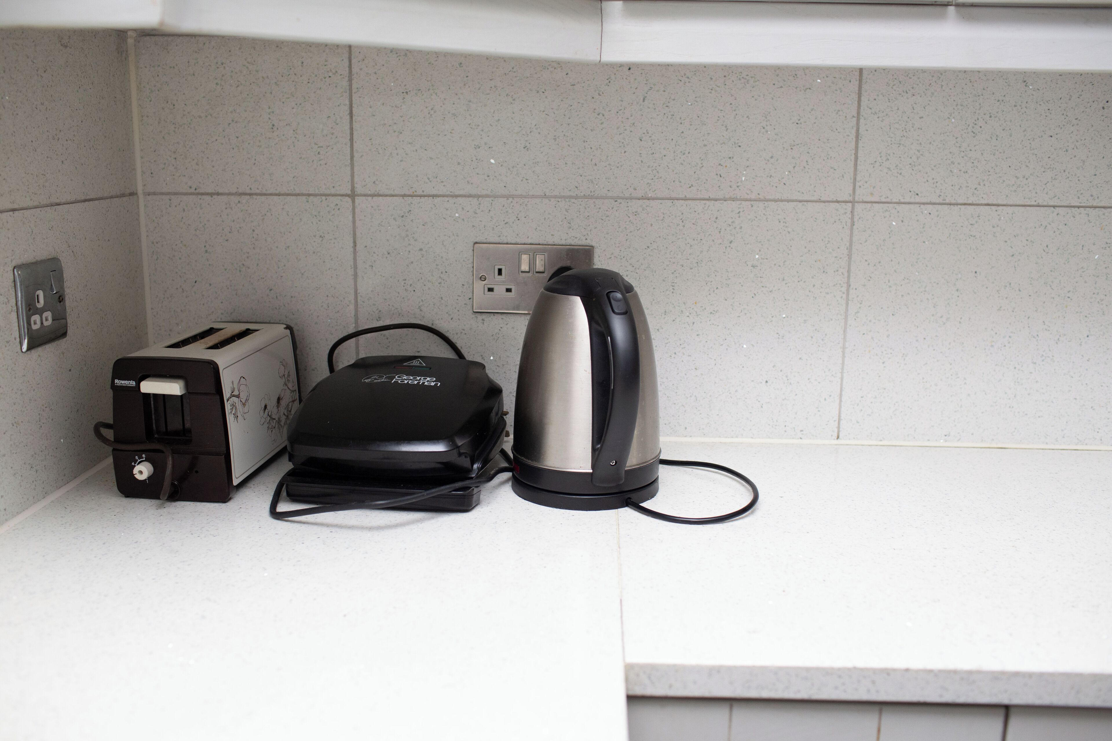 A kitchen counter with a toaster, a kettle, and a power strip.