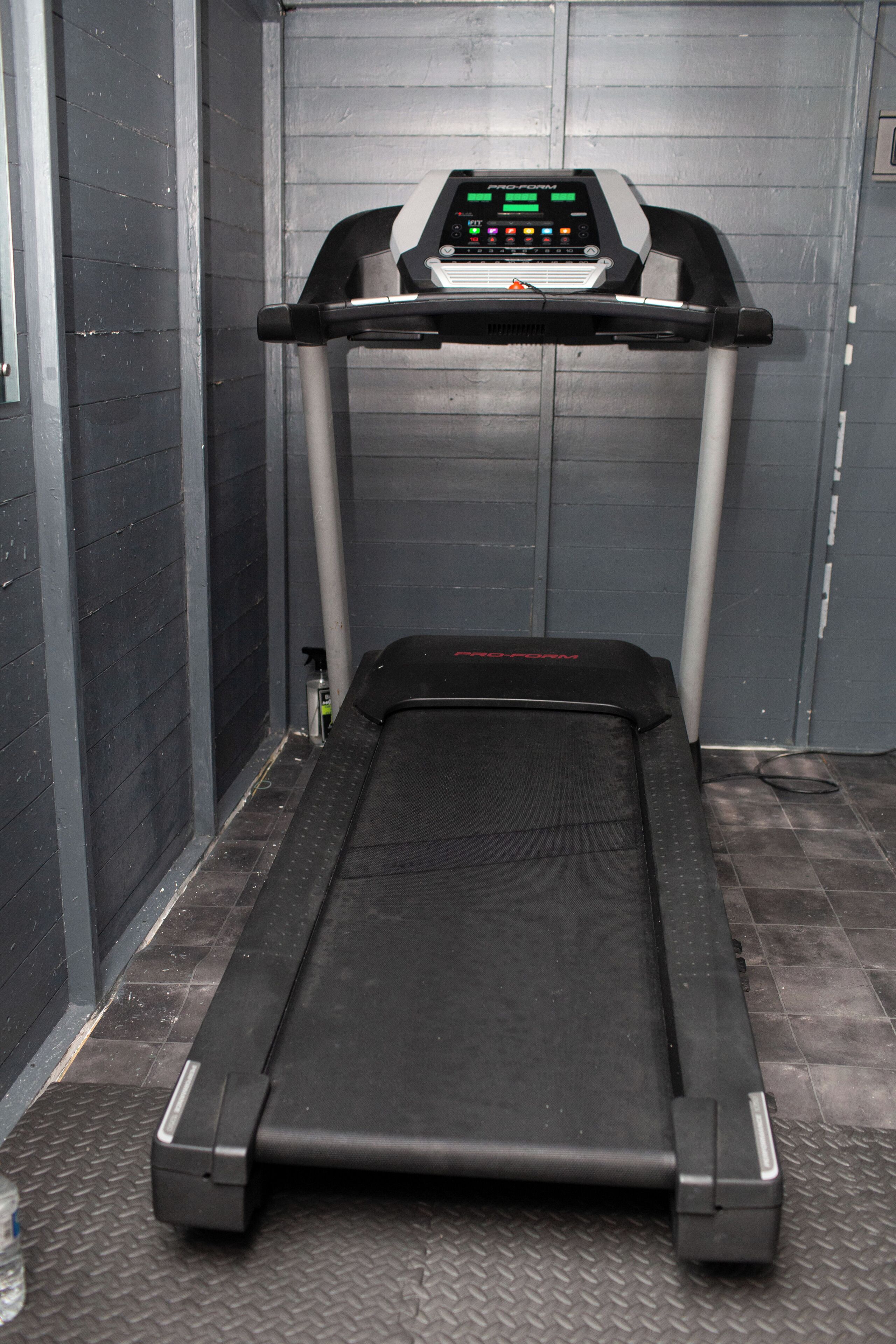 A treadmill in a room with grey walls and a tiled floor.