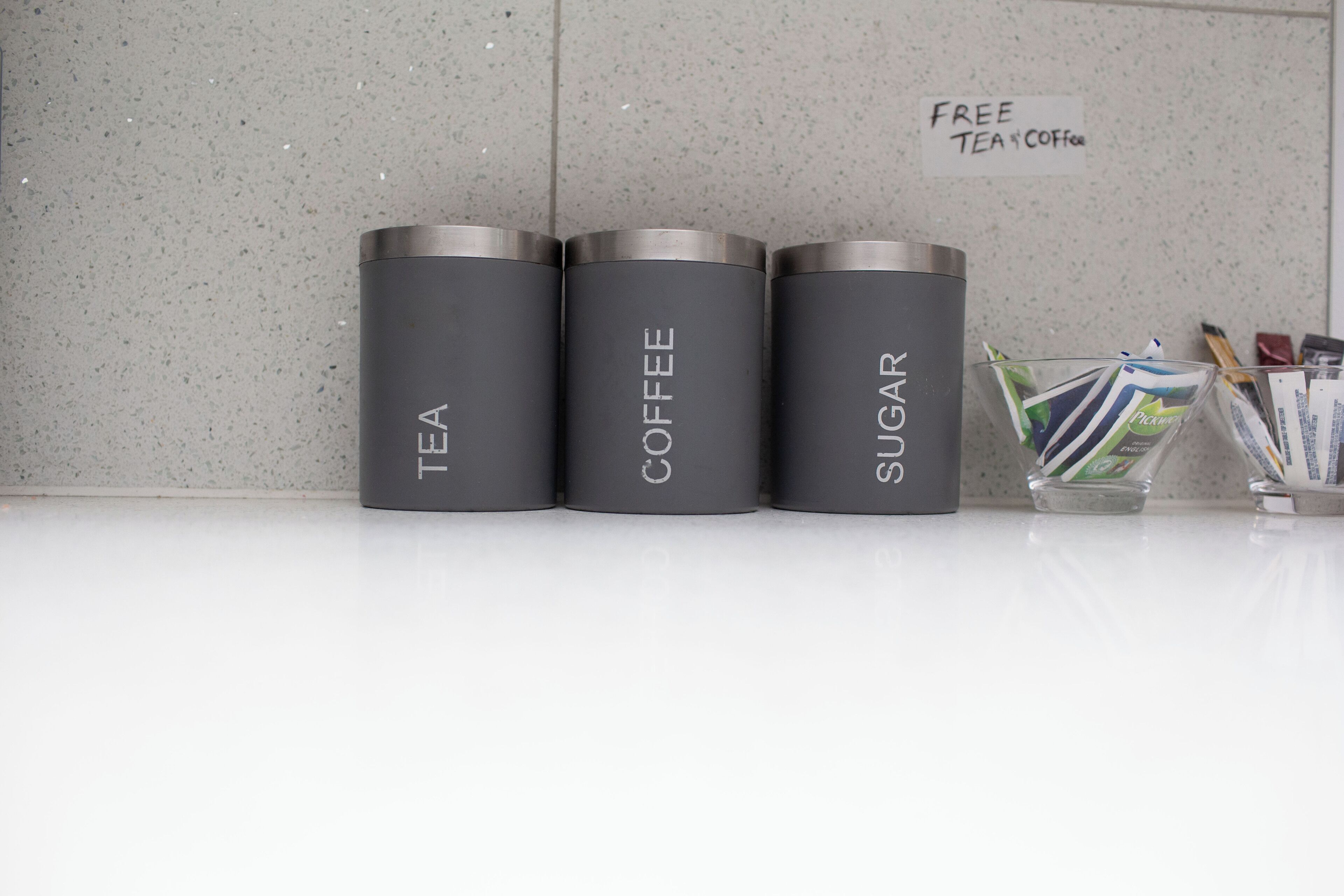 Three cylindrical containers labeled "TEA," "COFFEE," and "SUGAR" on a countertop.