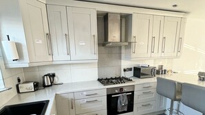 A modern kitchen with white cabinets, a gas stove, a microwave, and a bar stool. - The Grey Mansion near Manchester City Stadium, Co-Ops LIVE, Piccadilly... (Manchester)