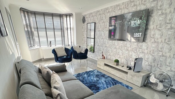 A modern living room with a grey sectional sofa, a blue armchair, and a flat-screen TV mounted on a textured wall. - The Grey Mansion near Manchester City Stadium, Co-Ops LIVE, Piccadilly... (Manchester)