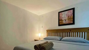 Habitació d'hotel amb un llit, una nit, una làmpada i un quadre d'una escena de parc.