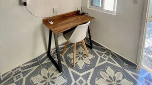 Habitació petita amb escriptori de fusta, cadira blanca, terra amb disseny i un aparell d'aire condicionat.