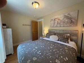 Un dormitorio con una cama grande, cabecera de madera, un cuadro en la pared y una mesita de noche con una lámpara.