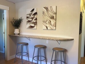 A kitchen area with a countertop, three stools, and two wall-mounted artworks.