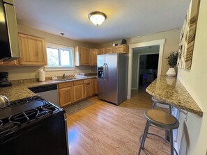 Una cocina con armarios de madera, un refrigerador de acero inoxidable, una estufa a gas y un taburete de bar.