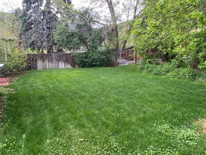 A well-maintained grassy backyard with a wooden fence, trees, and a small shed.