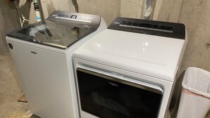 Due elettrodomestici Whirlpool, una lavatrice e un'asciugatrice, affiancati in una stanza con pavimento in cemento e parete in legno.