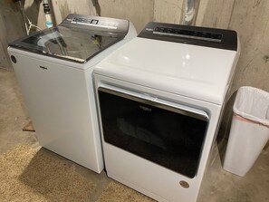 Two Whirlpool appliances, a washer and a dryer, placed next to each other in a room with a concrete floor and a wooden wall.
