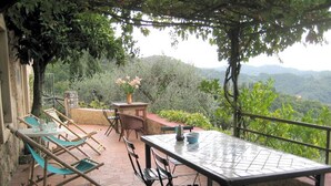 Une terrasse extérieure avec une table et des chaises, entourée de verdure et offrant une vue sur un paysage montagneux.