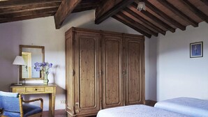 Une chambre avec une armoire en bois, un bureau avec un miroir et un lit recouvert d’une courtepointe blanche.