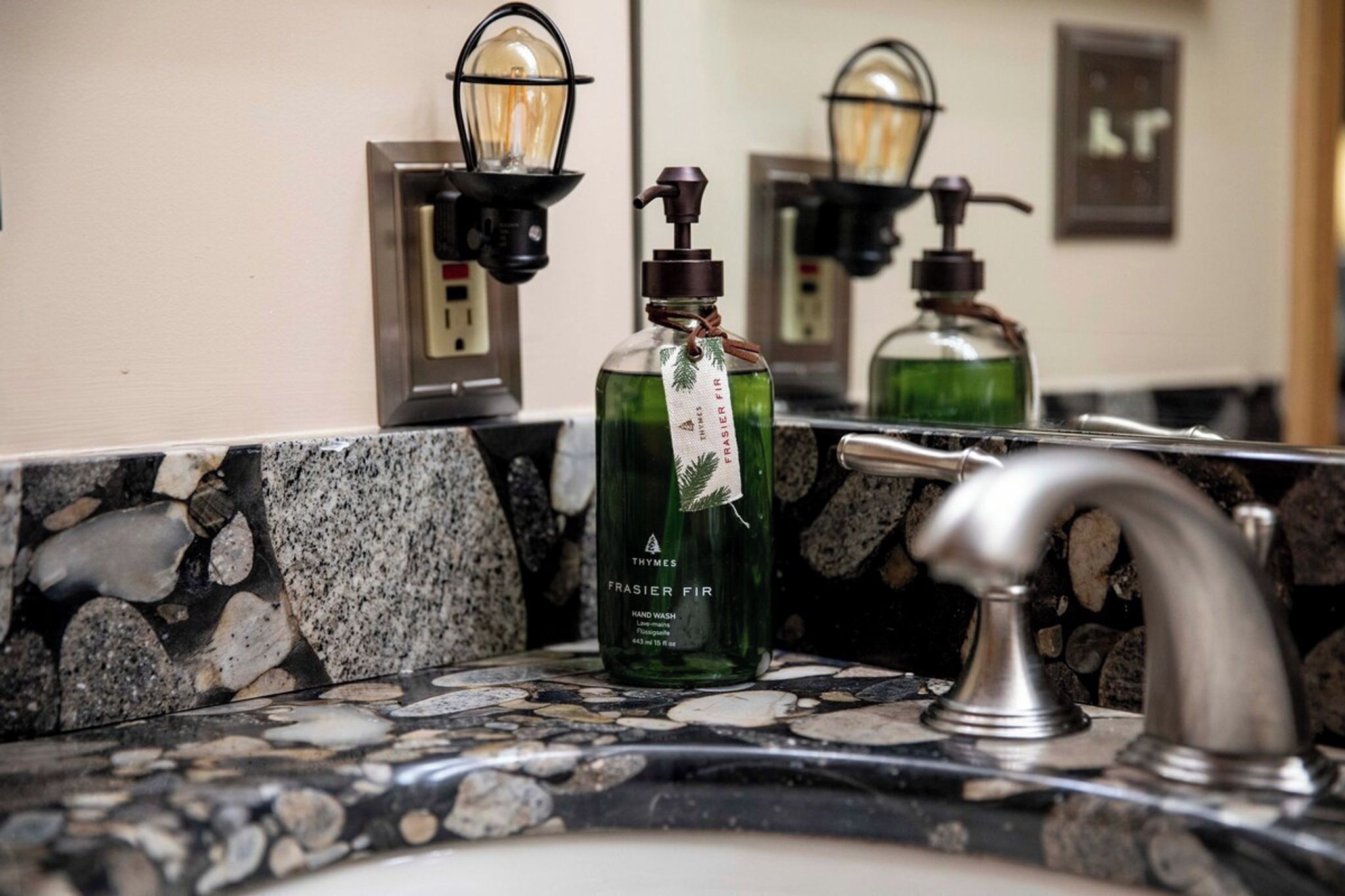 A bathroom with a granite countertop, a green hand soap dispenser, and a faucet.