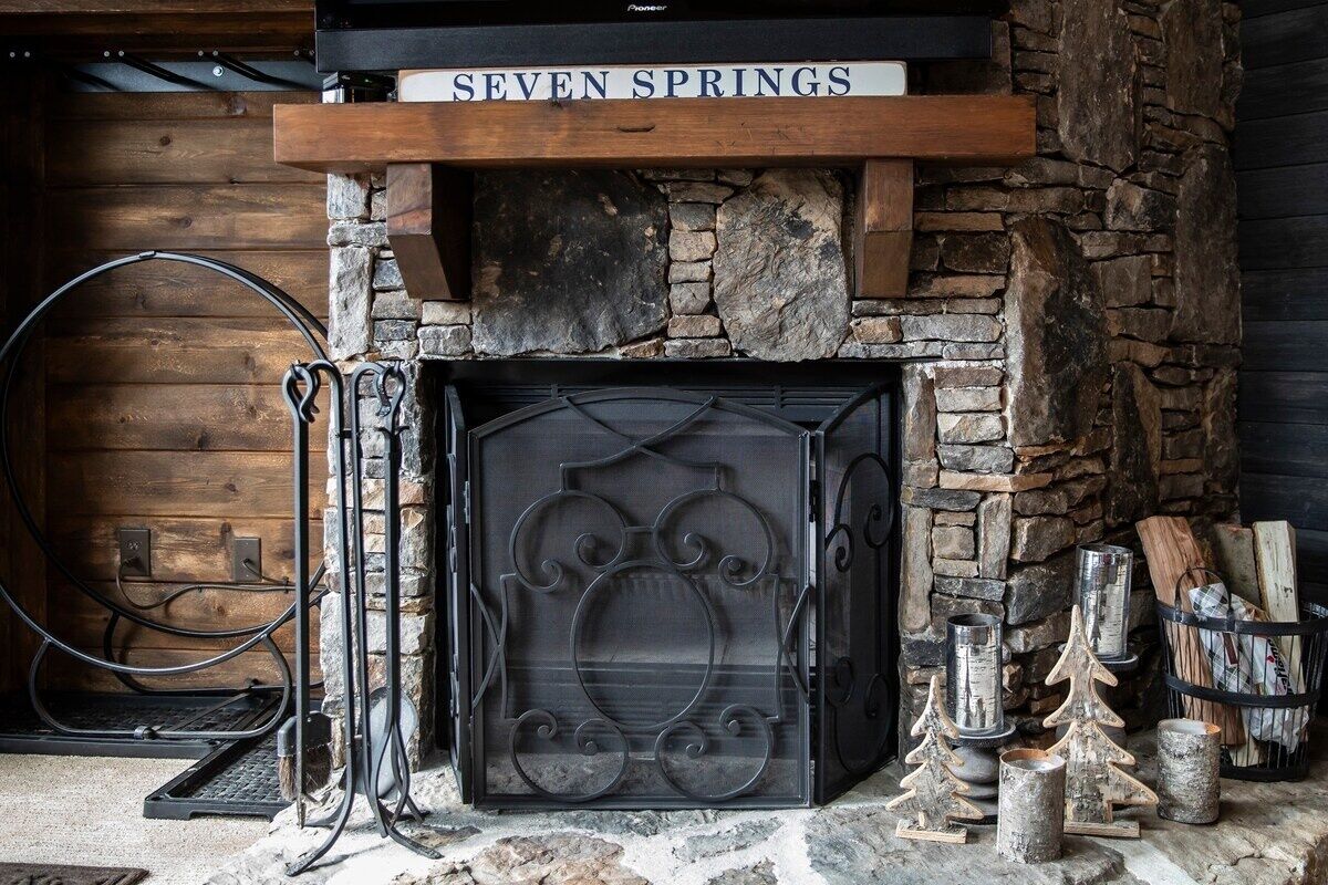 A stone fireplace with a metal grate, surrounded by logs and decorative trees.