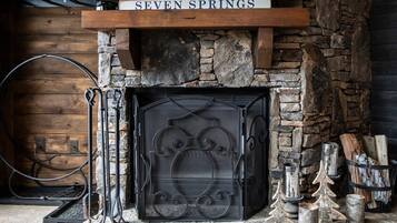 A stone fireplace with a metal grate, surrounded by logs and decorative trees.