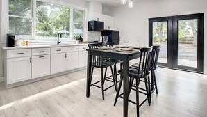 A modern kitchen with white cabinets, a black dining table, and a large window. - Cozy Getaway Home Near Siesta Key Beach  (Sarasota)