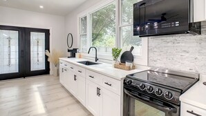 A modern kitchen with white cabinetry, a black stove, and a large window. - Cozy Getaway Home Near Siesta Key Beach  (Sarasota)