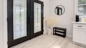 A modern interior with black-framed glass doors, a white wall, a round mirror, a small table with pampas grass, and a coffee maker on a white countertop. - Cozy Getaway Home Near Siesta Key Beach  (Sarasota)