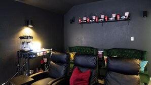 A dark-themed room with a green upholstered couch, two black leather chairs, a popcorn machine, and a shelf with snacks. - 🏈 GAME DAY WATCH PARTY!  (Bryan)