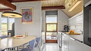 A modern kitchen with a dining area, featuring a large window, a painting, and a coffee machine. - Cozy home in Harboøre with WiFi (Harboøre)
