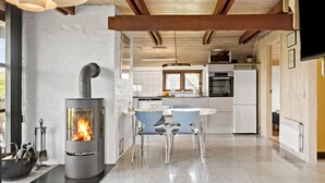 A modern kitchen with a wood-burning stove, a dining area with chairs, and a kitchen island. - Cozy home in Harboøre with WiFi (Harboøre)