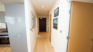 Un couloir au sol en bois, avec un coin cuisine sur la gauche et une porte au fond.