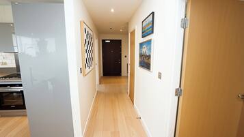 A hallway with wooden flooring, a kitchen area on the left, and a door at the end.