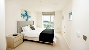 Une chambre à coucher moderne, avec un lit, des tables de chevet, une fenêtre donnant sur un beau paysage et un tableau accroché au mur.