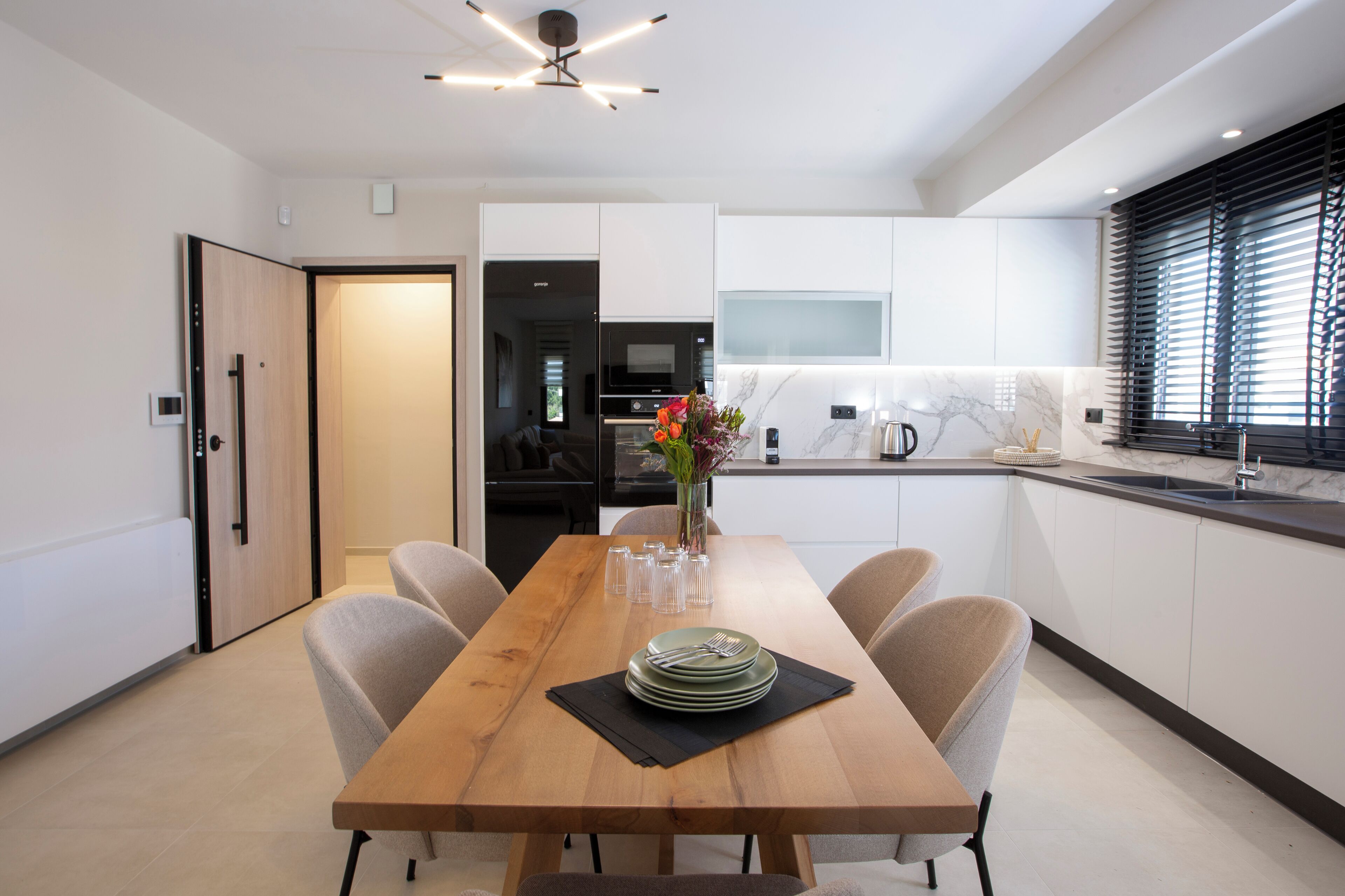 Una cocina moderna con armarios blancos, una mesa de comedor de madera y un horno empotrado.