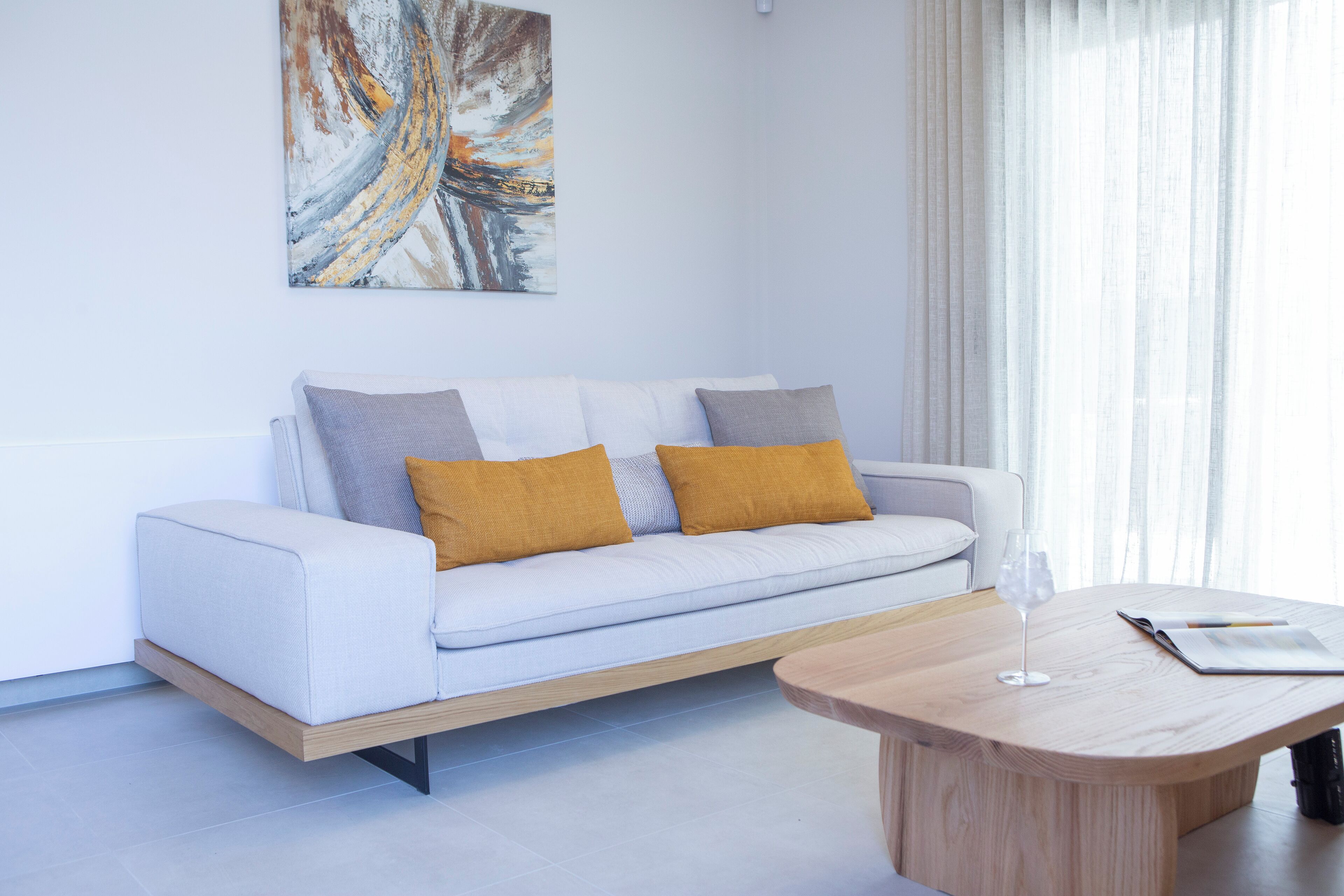 A modern living room with a white sofa, two mustard-colored cushions, a wooden coffee table, and a glass of water.