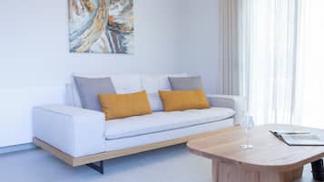 A modern living room with a white sofa, two mustard-colored cushions, a wooden coffee table, and a glass of water.