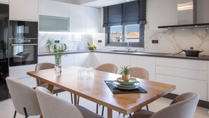 A modern kitchen with built-in appliances, a dining table with chairs, and a window with blinds. - Pomaria Boutique Residences (Lefkada)