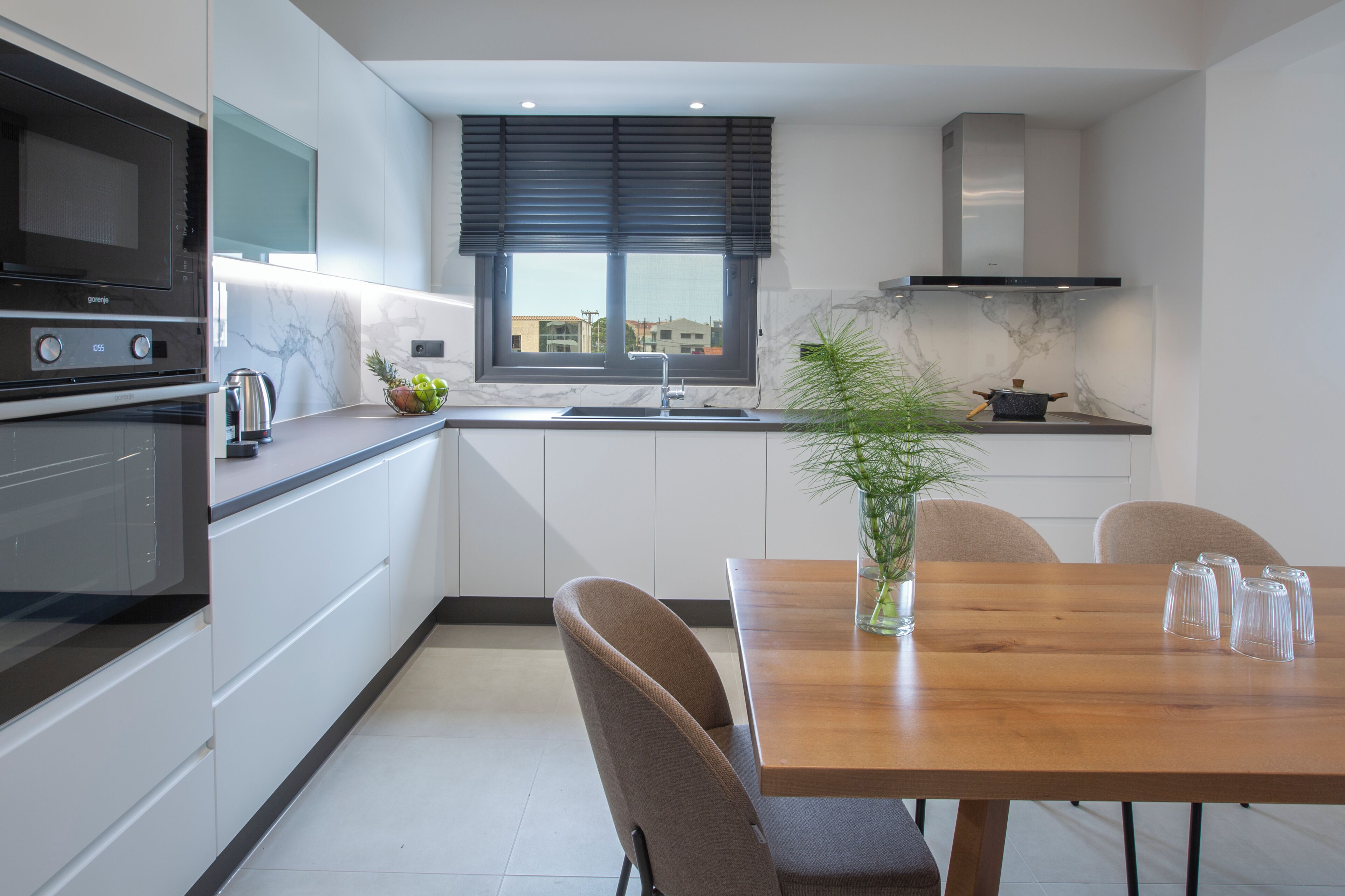 Een moderne keuken met een inbouwoven, magnetron en kookplaat. Er staat een eettafel met stoelen en een vaas met groen.