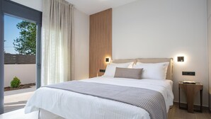 A modern hotel room with a large bed, two bedside tables, and a view of the outdoors. - Pomaria Boutique Residences (Lefkada)