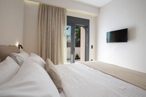 A modern hotel room with a large bed, a flat-screen TV mounted on the wall, and a sliding glass door leading to an outdoor area. - Pomaria Boutique Residences (Lefkada)