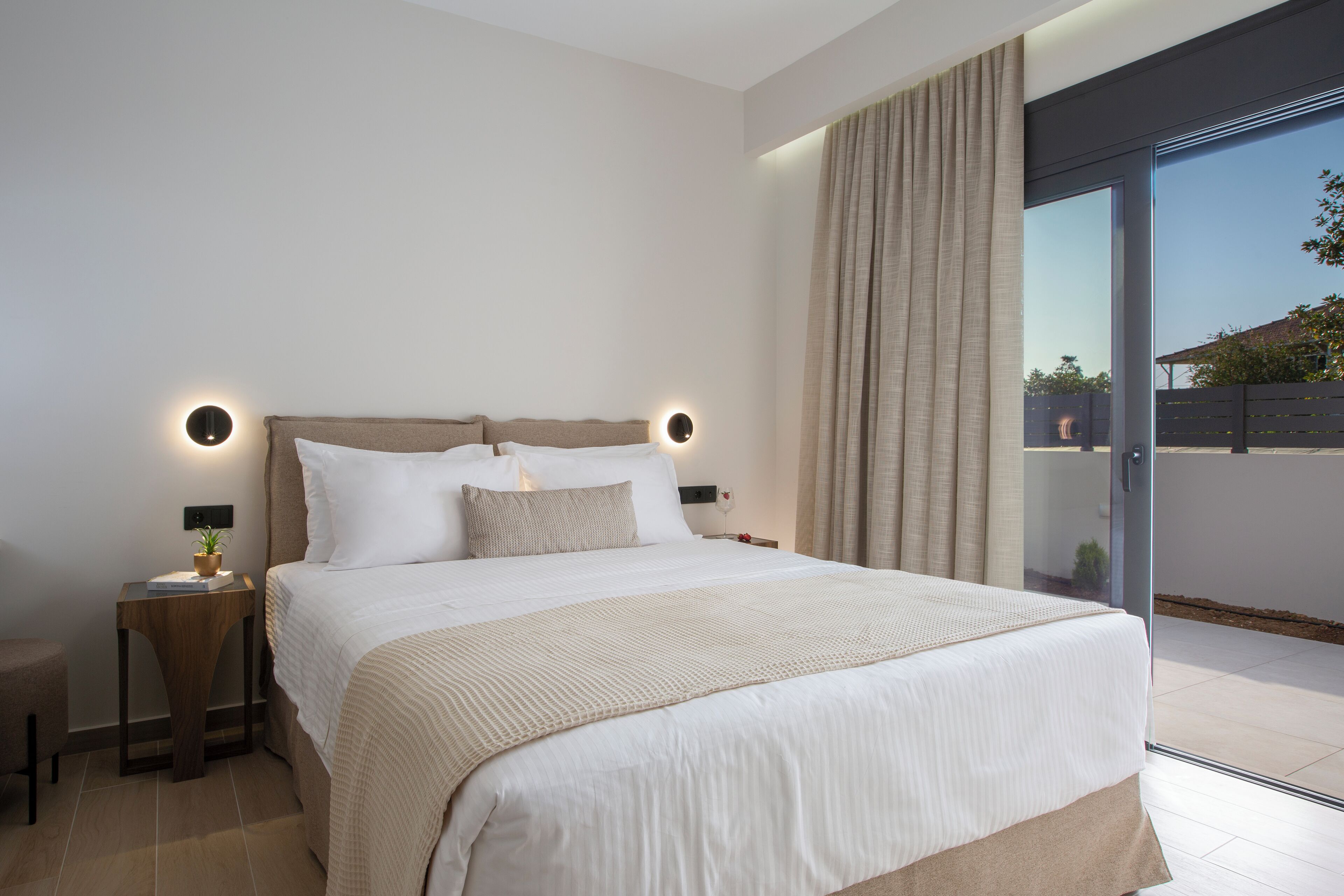 A modern bedroom with a large bed, two bedside tables, a nightstand, and a sliding glass door to a balcony.