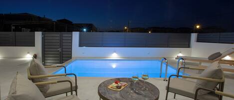 A rooftop pool area with lounge chairs, a table with food and drinks, and a clear view of the pool.