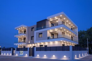 A modern multi-story building with balconies, a gated entrance, and exterior lighting. - Pomaria Residences (Lefkada)