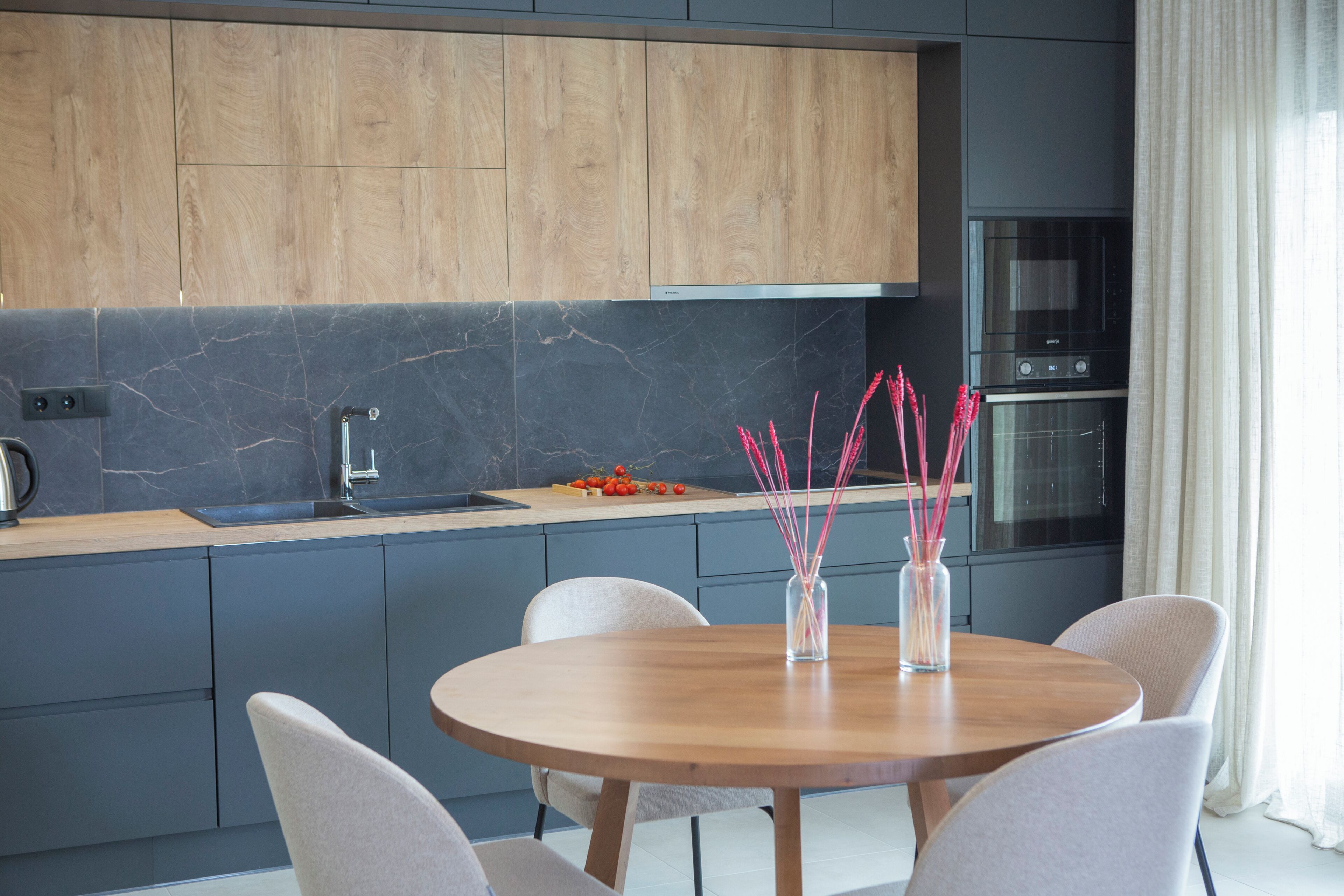 A modern kitchen with grey cabinets, a wooden dining table, and a built-in oven.