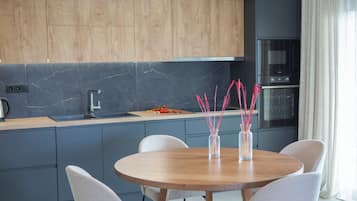 A modern kitchen with grey cabinets, a wooden dining table, and a built-in oven.