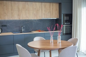 A modern kitchen with grey cabinets, a wooden dining table, and a built-in oven. - Pomaria Boutique Residences (Lefkada)