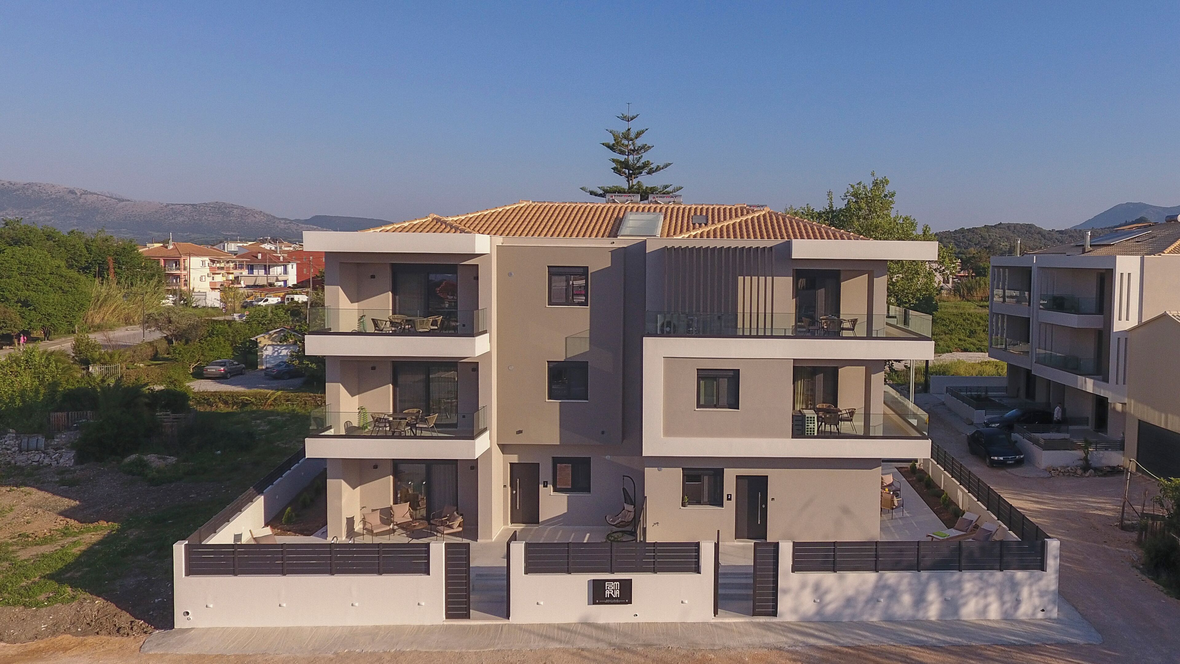 A multi-story residential building with balconies, a gated entrance, and a view of the surrounding landscape.