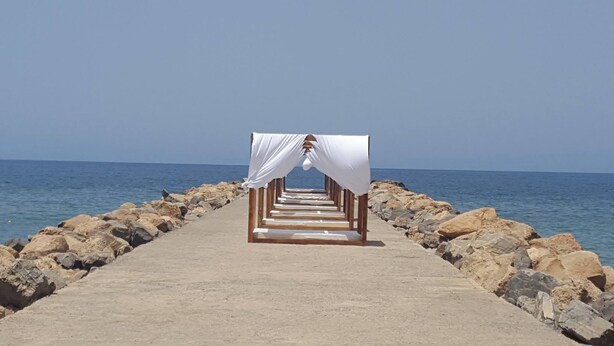A concrete pathway leading to a white gazebo by the sea.