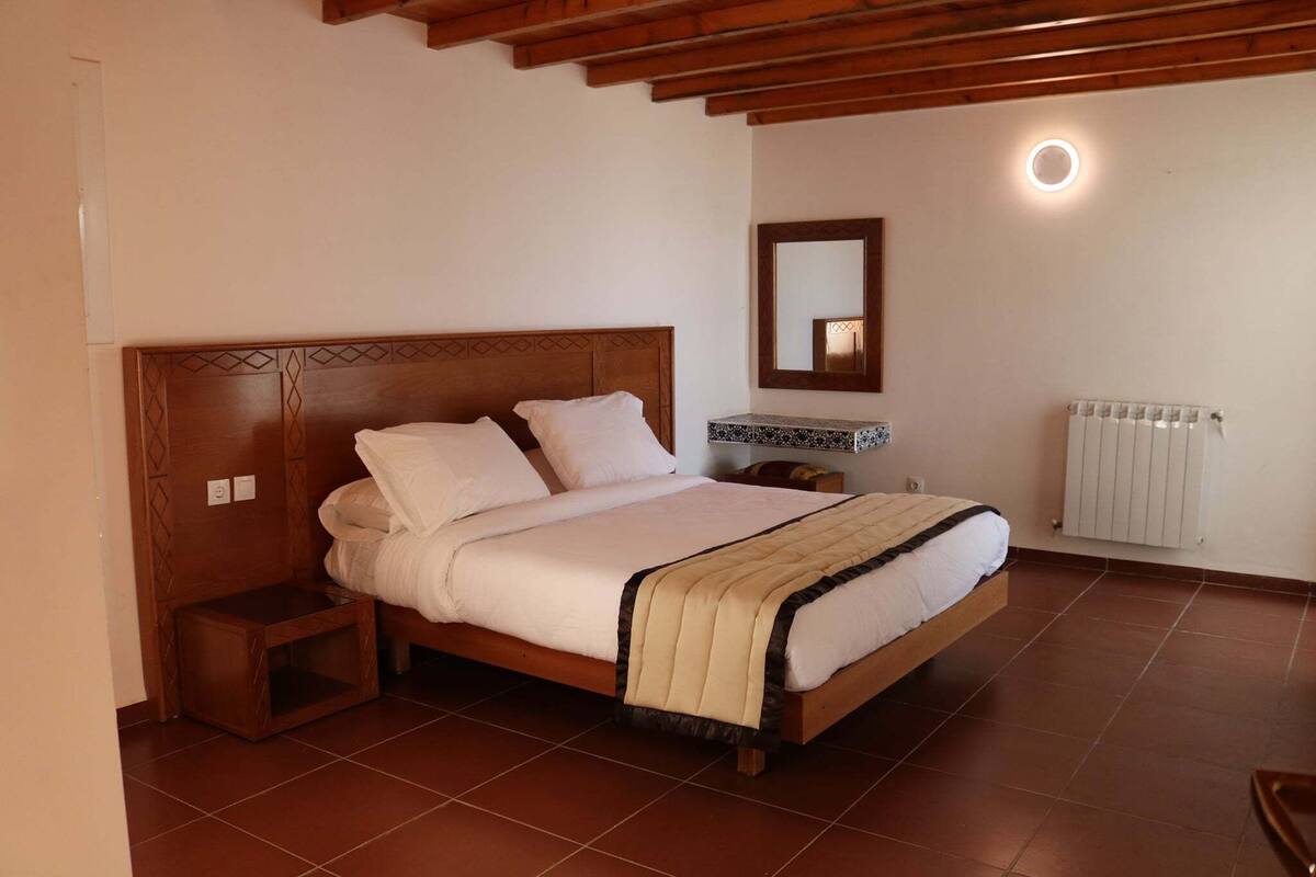 Ein Schlafzimmer mit einem hölzernen Bett, einem Nachttisch, einem Heizkörper und einem Spiegel.