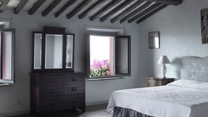 Een slaapkamer met een bed, een dressoir, een raam met uitzicht op roze bloemen en een lamp op een nachtkastje.