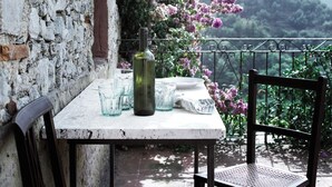 Een tafel buiten gedekt, met een fles en glazen, omringd door een tuin met roze bloemen en een uitzicht op heuvels.