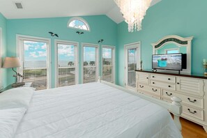 Een slaapkamer met een groot bed, een televisie, een kroonluchter en een uitzicht op de lucht door de ramen.