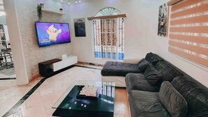 Ein modernes Wohnzimmer mit großem Fernseher, einer Kristallleuchtre, einer Couch und einem Couchtisch.